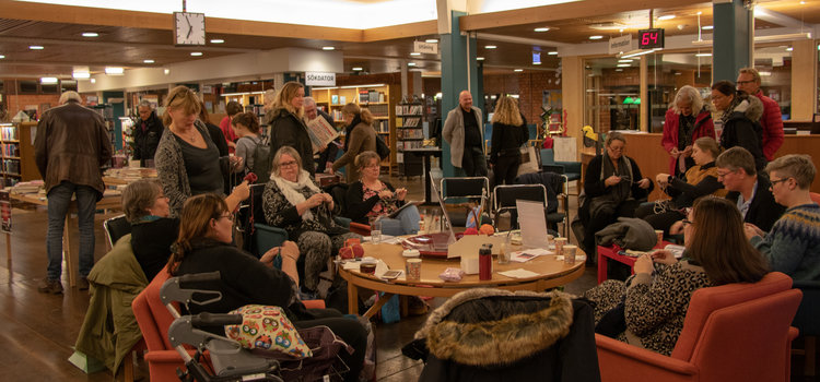 folk som sitter runt ett runtbord, pratar och stickar