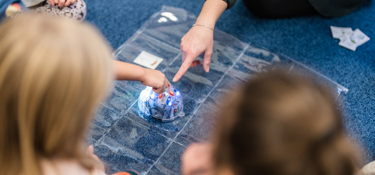 En pedagog och fler barn som pekar på en mini robot som lyser på golvet 