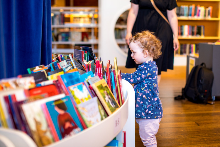 Två barn och en vuxen som sitter på ett bibliotek och tittar på en bok