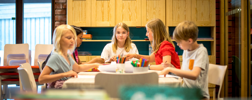 En pedagog och fler barn som pekar på en mini robot som lyser på golvet 