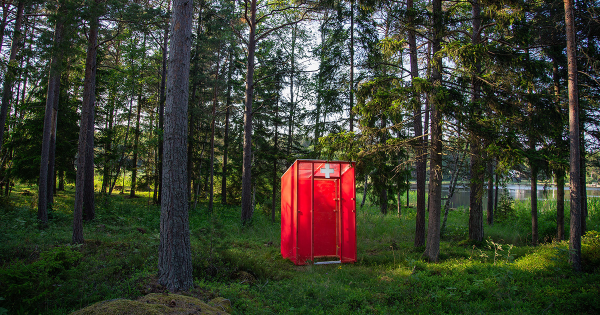 ett rött litet skjul med ett vitt kors står i skogen.